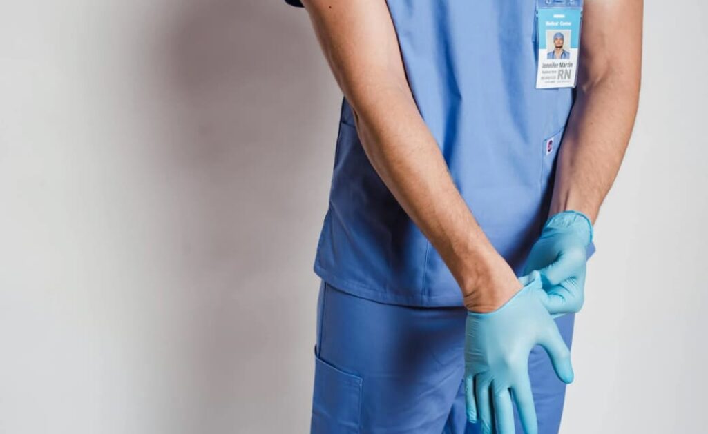 Healthcare worker in blue scrubs putting on gloves