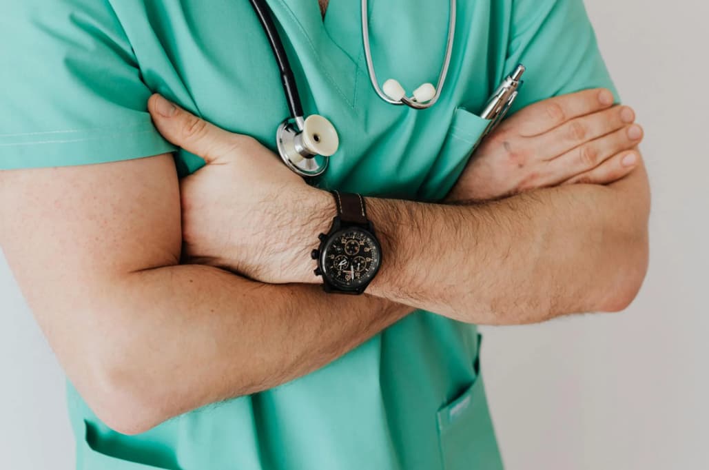 Healthcare professional in teal scrubs with arms crossed and a watch