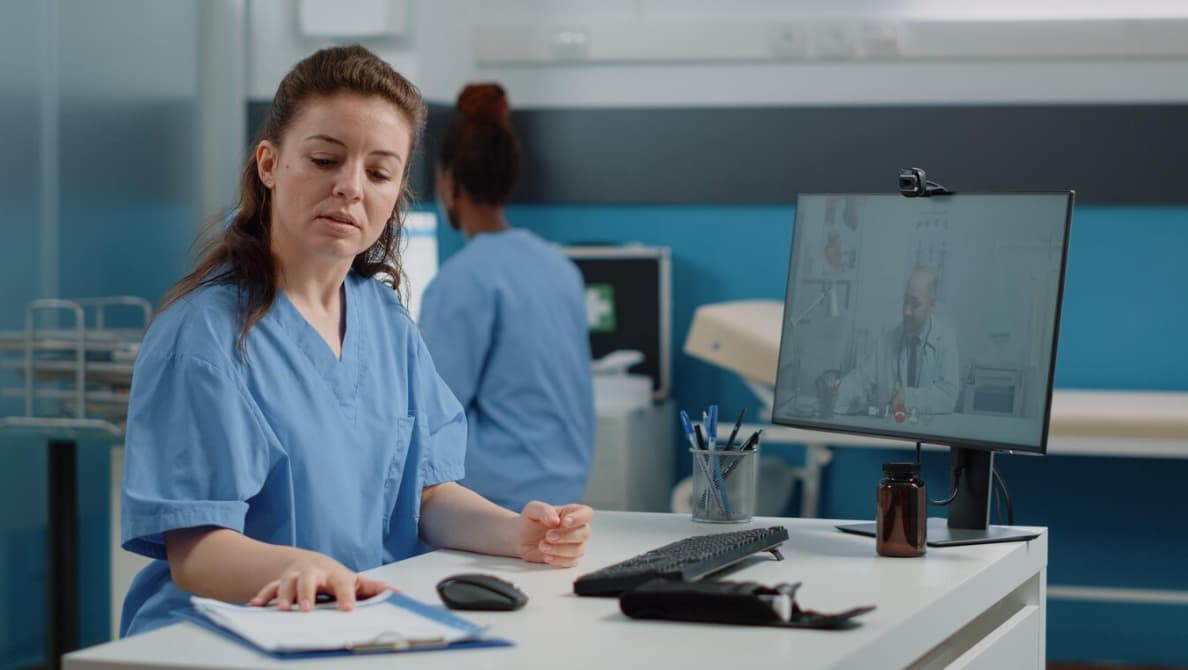 A nurse reviews notes during a virtual consultation with a doctor