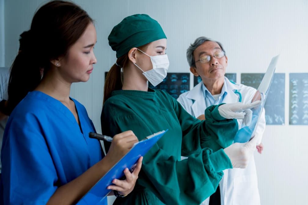 Three healthcare professionals discuss over an X-ray in a clinic