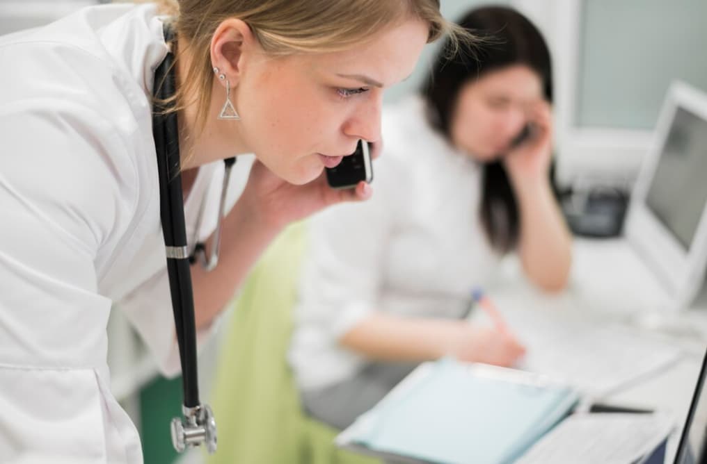 A healthcare professional speaks on the phone while looking at a document