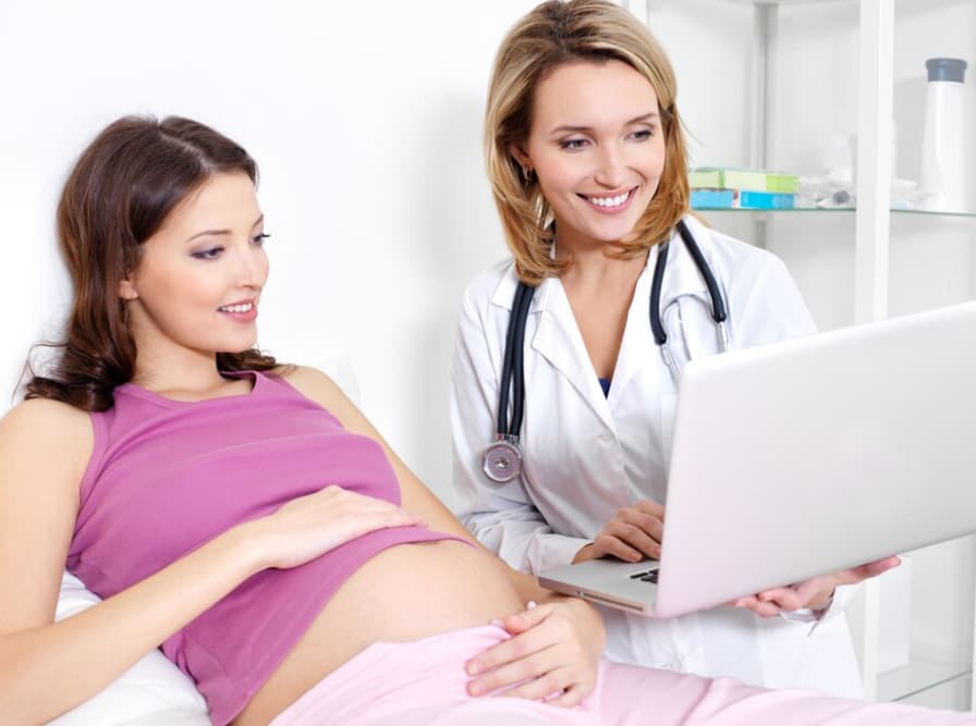 A smiling pregnant patient with her doctor holding a laptop
