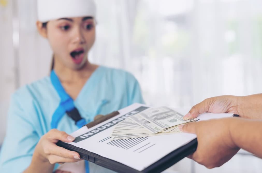 A nurse looks shocked receiving cash over an insurance clipboard