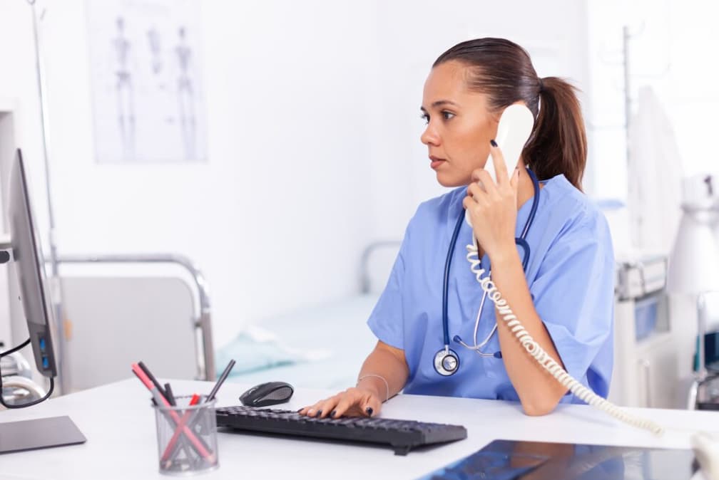 A focused nurse speaks on the phone at her desk