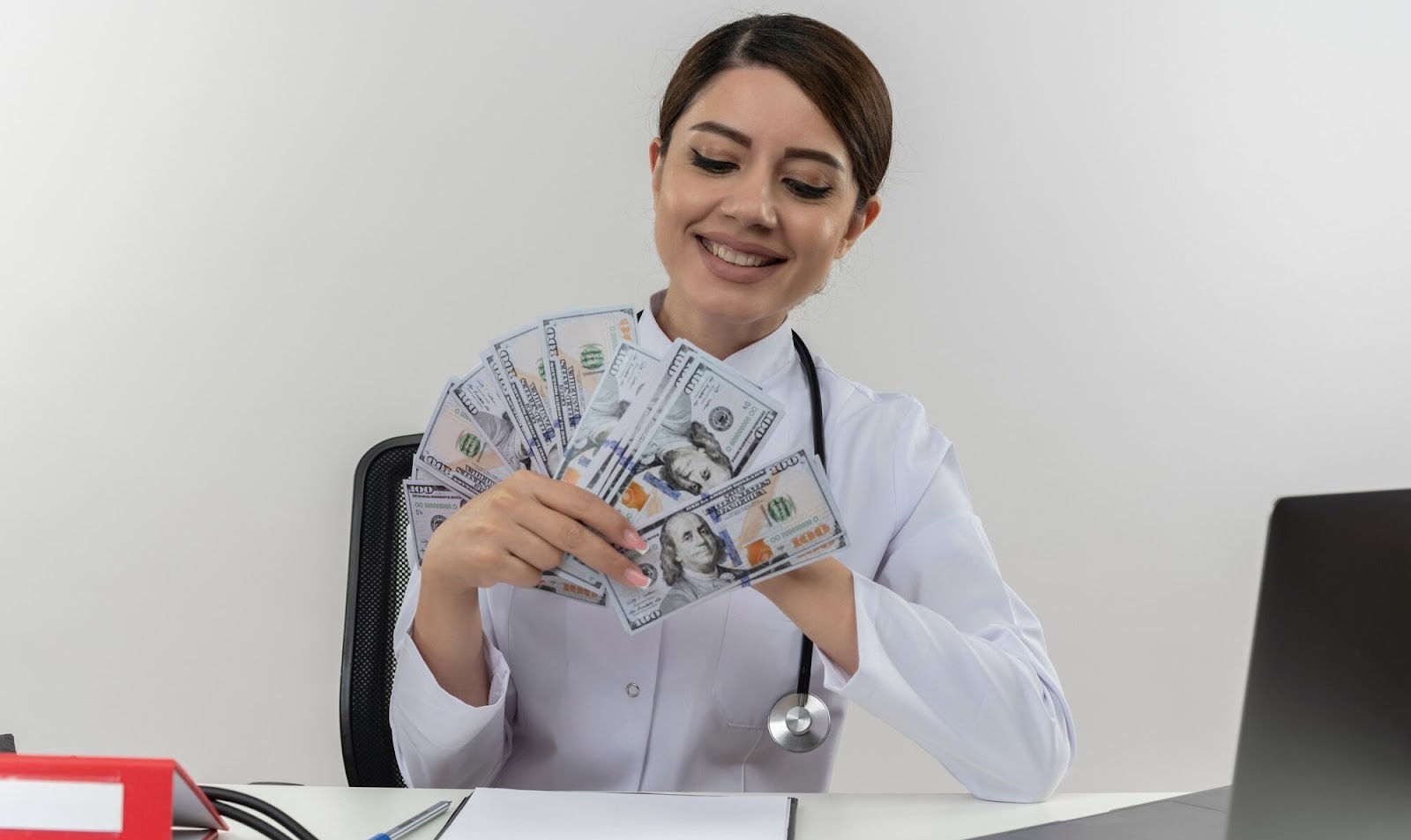 A female doctor in a medical gown and a stethoscope sits at the table and holds money in her hands