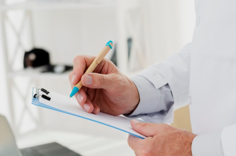 Close-up of a doctor's hand writing on a clipboard