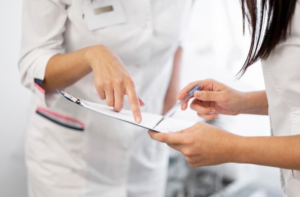 Two healthcare workers discussing over a clipboard in a hospital