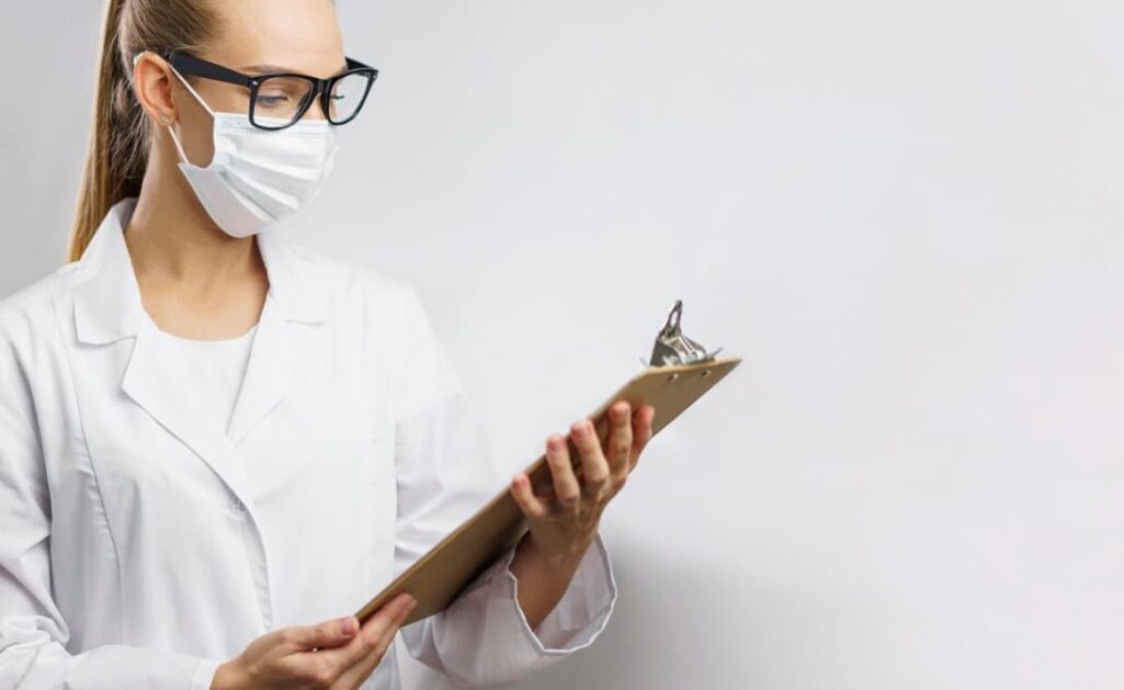 A focused female doctor in glasses and a mask reviewing a document
